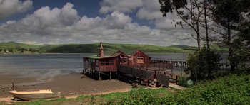 Movie still from “The Fog” (1980), directed by John Carpenter – A wooden house on the shore of a body of water; Extreme Wide shot, Low angle