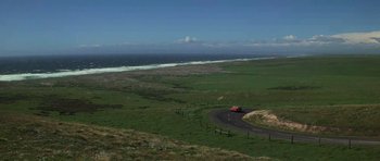 Movie still from “The Fog” (1980), directed by John Carpenter – A red truck driving down a road next to the ocean; Extreme Wide shot, High angle