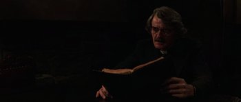 Movie still from “The Fog” (1980), directed by John Carpenter – An older man in a priest's outfit reading a book; Close Up shot, Low angle
