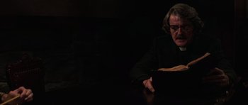 Movie still from “The Fog” (1980), directed by John Carpenter – A person sitting at a table with a book; Medium shot, Low angle