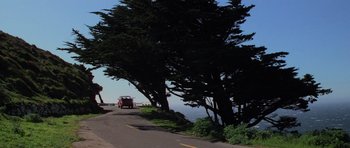 Movie still from “The Fog” (1980), directed by John Carpenter – A car driving down a road next to a body of water; Extreme Wide shot, Low angle