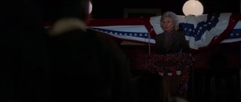 Movie still from “The Fog” (1980), directed by John Carpenter – An older woman standing in front of an american flag; Medium shot, Low angle