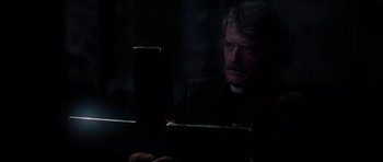 Movie still from “The Fog” (1980), directed by John Carpenter – A man in a priest's outfit looking at a tablet computer in the dark; Close Up shot, Over the shoulder angle