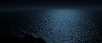 Movie still from “The Fog” (1980), directed by John Carpenter – A body of water at night lit up by the lights; Extreme Wide shot, High angle