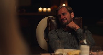 Movie still from “The Forever Purge” (2021), directed by Everardo Gout – A man sitting at a table in a leather chair; Medium shot, Over the shoulder angle