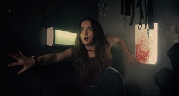 Movie still from “The Forever Purge” (2021), directed by Everardo Gout – A woman with long brown hair is in a dark room; Medium shot, Low angle