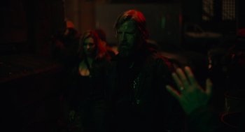 Movie still from “The Forever Purge” (2021), directed by Everardo Gout – A man with a long beard is standing next to a woman in a dark room; Medium shot, Over the shoulder angle
