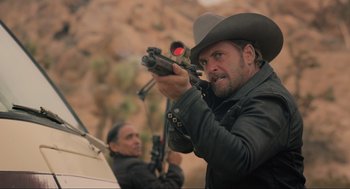 Movie still from “The Forever Purge” (2021), directed by Everardo Gout – A man in a cowboy hat holding a rifle; Medium shot, Over the shoulder angle