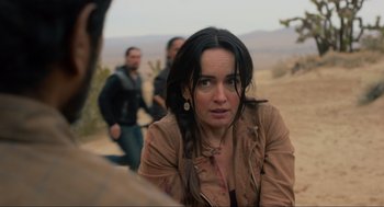 Movie still from “The Forever Purge” (2021), directed by Everardo Gout – A woman sitting on the side of a dirt road next to two men; Close Up shot, Over the shoulder angle