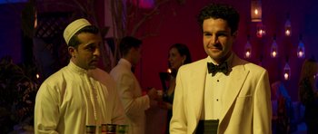 Movie still from “The Forgiven” (2021), directed by John Michael McDonagh – A man in a white suit standing next to a woman in a white suit; Medium shot, Over the shoulder angle