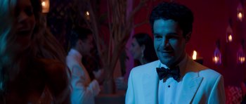 Movie still from “The Forgiven” (2021), directed by John Michael McDonagh – A man in a white suit and a bow tie; Medium shot, Over the shoulder angle