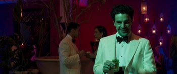 Movie still from “The Forgiven” (2021), directed by John Michael McDonagh – A man in a white tuxedo holding a drink; Medium shot, Over the shoulder angle