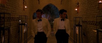 Movie still from “The Forgiven” (2021), directed by John Michael McDonagh – Two men in tuxedos standing next to each other in front of an archway; Medium shot, Over the shoulder angle