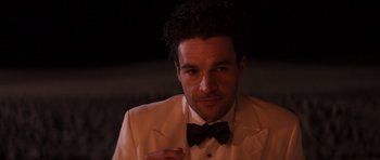 Movie still from “The Forgiven” (2021), directed by John Michael McDonagh – A person wearing a suit and bow tie; Close Up shot, Over the shoulder angle