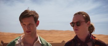 Movie still from “The Forgiven” (2021), directed by John Michael McDonagh – Two men standing next to each other in the desert; Close Up shot, Over the shoulder angle