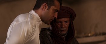 Movie still from “The Forgiven” (2021), directed by John Michael McDonagh – A man and a man wearing a head covering; Close Up shot, Over the shoulder angle