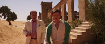 Movie still from “The Forgiven” (2021), directed by John Michael McDonagh – A man and a man standing next to each other on a street; Medium shot, Over the shoulder angle