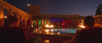 Movie still from “The Forgiven” (2021), directed by John Michael McDonagh – A group of people standing around a pool at night; Extreme Wide shot, High angle