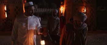 Movie still from “The Forgiven” (2021), directed by John Michael McDonagh – A group of men standing around a building at night; Medium shot, Over the shoulder angle