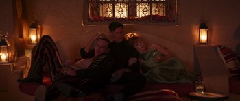 Movie still from “The Forgiven” (2021), directed by John Michael McDonagh – A group of people sitting next to each other on top of a couch; Medium shot, High angle