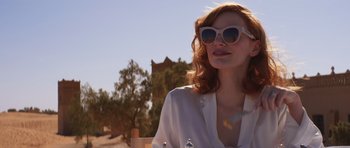 Movie still from “The Forgiven” (2021), directed by John Michael McDonagh – A woman wearing sunglasses standing in front of a building; Medium shot, Low angle