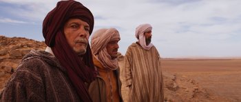 Movie still from “The Forgiven” (2021), directed by John Michael McDonagh – A group of men standing on top of a dirt field; Medium shot, Over the shoulder angle