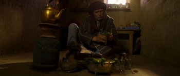 Movie still from “The Forgiven” (2021), directed by John Michael McDonagh – A man sitting on the ground with a bunch of food; Medium shot, Low angle