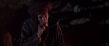 Movie still from “The Forgiven” (2021), directed by John Michael McDonagh – A man with a turban smoking a cigarette in the dark; Medium shot, Low angle