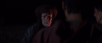 Movie still from “The Forgiven” (2021), directed by John Michael McDonagh – An older man wearing a turban and a red turban; Close Up shot, Over the shoulder angle