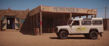 Movie still from “The Forgiven” (2021), directed by John Michael McDonagh – A truck parked in front of a store with clothes hanging on the roof; Wide shot, Over the shoulder angle