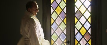 Movie still from “The Forgiven” (2021), directed by John Michael McDonagh – A man standing in front of a stained glass window; Medium shot, Low angle