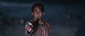 Movie still from “The Forgiven” (2021), directed by John Michael McDonagh – A young man holding a gun in his right hand; Close Up shot, Over the shoulder angle