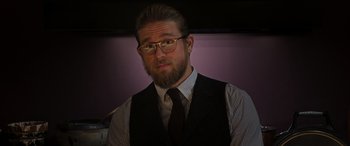 Movie still from “The Gentlemen” (2019), directed by Guy Ritchie – A man with a goatee and beard wearing glasses; Close Up shot, Over the shoulder angle