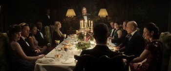 Movie still from “The Gentlemen” (2019), directed by Guy Ritchie – A group of people sitting around a dinner table; Medium shot, Over the shoulder angle