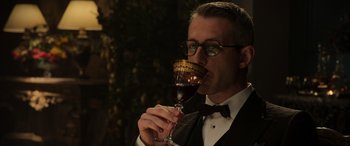 Movie still from “The Gentlemen” (2019), directed by Guy Ritchie – A man in a tuxedo drinking a glass of red wine; Close Up shot, Over the shoulder angle