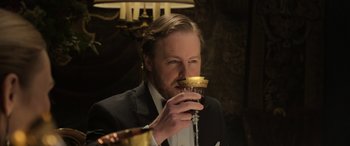 Movie still from “The Gentlemen” (2019), directed by Guy Ritchie – A man in a suit and tie drinking a glass of red wine; Close Up shot, Low angle