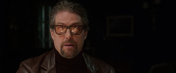 Movie still from “The Gentlemen” (2019), directed by Guy Ritchie – A person wearing glasses and a leather jacket; Close Up shot, Low angle