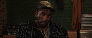 Movie still from “The Gentlemen” (2019), directed by Guy Ritchie – A man wearing a striped jacket and a hat; Close Up shot, High angle