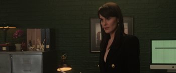 Movie still from “The Gentlemen” (2019), directed by Guy Ritchie – A woman standing in front of a lamp in front of a brick wall; Medium shot, Over the shoulder angle