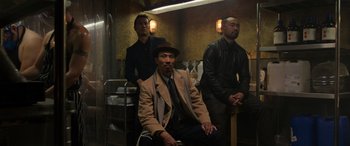 Movie still from “The Gentlemen” (2019), directed by Guy Ritchie – A group of men sitting on a chair in a dimly - lit room; Medium shot, Low angle