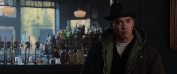 Movie still from “The Gentlemen” (2019), directed by Guy Ritchie – A man wearing a hat and a jacket in front of a bar; Close Up shot, Low angle