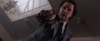 Movie still from “The Gentlemen” (2019), directed by Guy Ritchie – A man in a suit and tie holding a video game controller; Close Up shot, Low angle