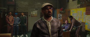 Movie still from “The Gentlemen” (2019), directed by Guy Ritchie – A man wearing a hat and glasses in a room; Medium shot, Over the shoulder angle