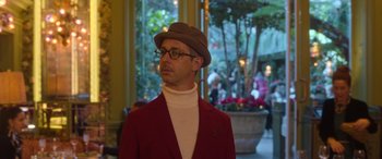 Movie still from “The Gentlemen” (2019), directed by Guy Ritchie – A man in a red jacket wearing glasses and a brown hat; Medium shot, Low angle