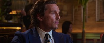 Movie still from “The Gentlemen” (2019), directed by Guy Ritchie – A person wearing a suit and tie; Close Up shot, Over the shoulder angle