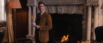 Movie still from “The Gentlemen” (2019), directed by Guy Ritchie – A man standing in front of a fireplace holding a plate; Medium shot, Low angle