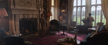 Movie still from “The Gentlemen” (2019), directed by Guy Ritchie – A man standing in a living room next to a fire place; Wide shot, Over the shoulder angle