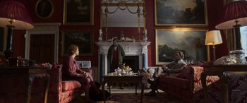 Movie still from “The Gentlemen” (2019), directed by Guy Ritchie – Two people sitting in front of a fireplace in a living room; Wide shot, Over the shoulder angle