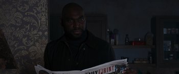 Movie still from “The Gentlemen” (2019), directed by Guy Ritchie – A man is reading a newspaper in a dark room; Close Up shot, Low angle