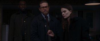 Movie still from “The Gentlemen” (2019), directed by Guy Ritchie – A man and a woman standing next to each other in a dark room; Medium shot, Over the shoulder angle